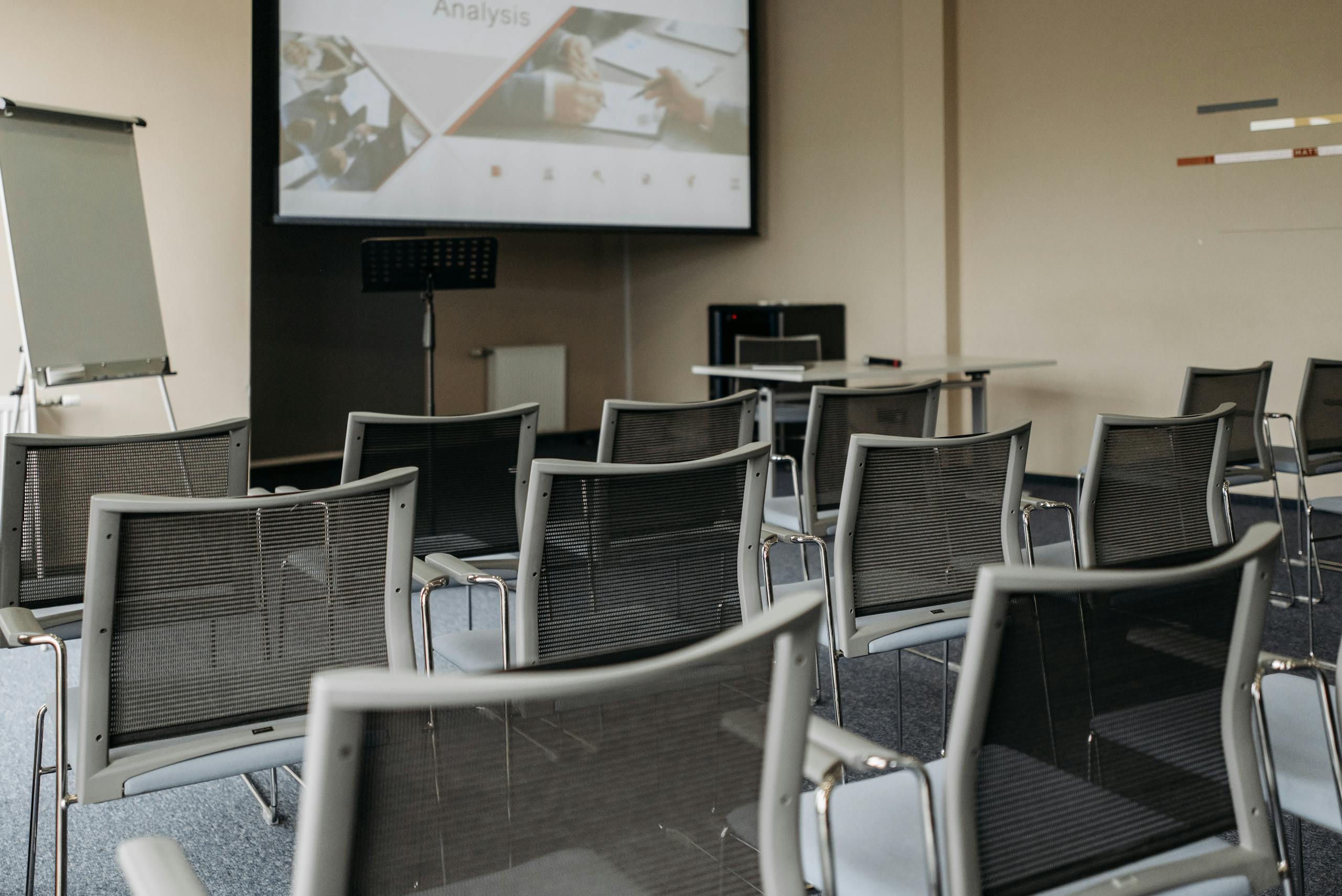 Modern conference room setup with empty chairs, projector screen, and presentation equipment.